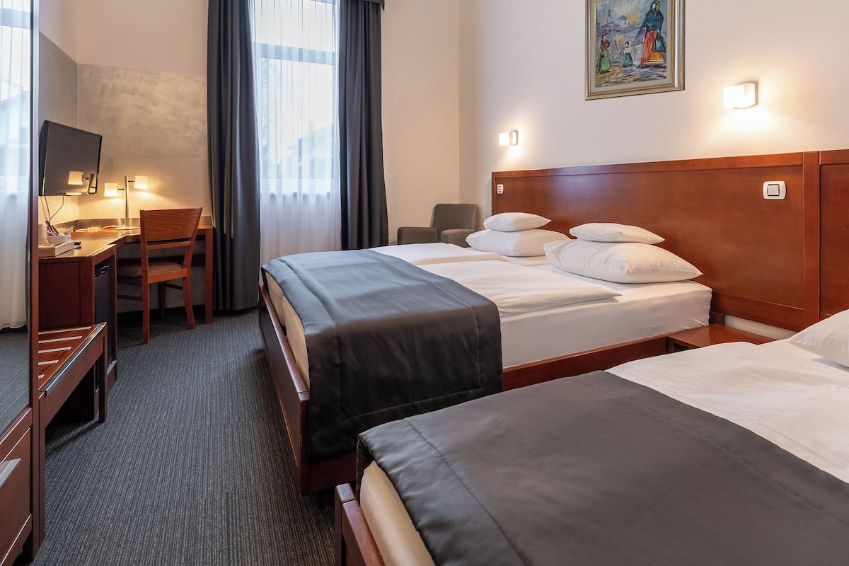 Una habitación de hotel con dos camas, un escritorio con una silla, un televisor y un cuadro en la pared.