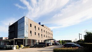 A modern building with a flat facade, multiple windows, and a parking lot with several cars.