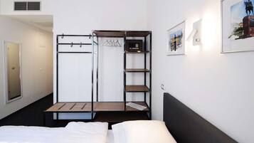A compact hotel room with a bed, a wardrobe with shelves, a mirror, and a framed picture on the wall.