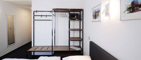 Habitación de hotel pequeña con cama, armario con estantes, espejo y un cuadro en la pared.