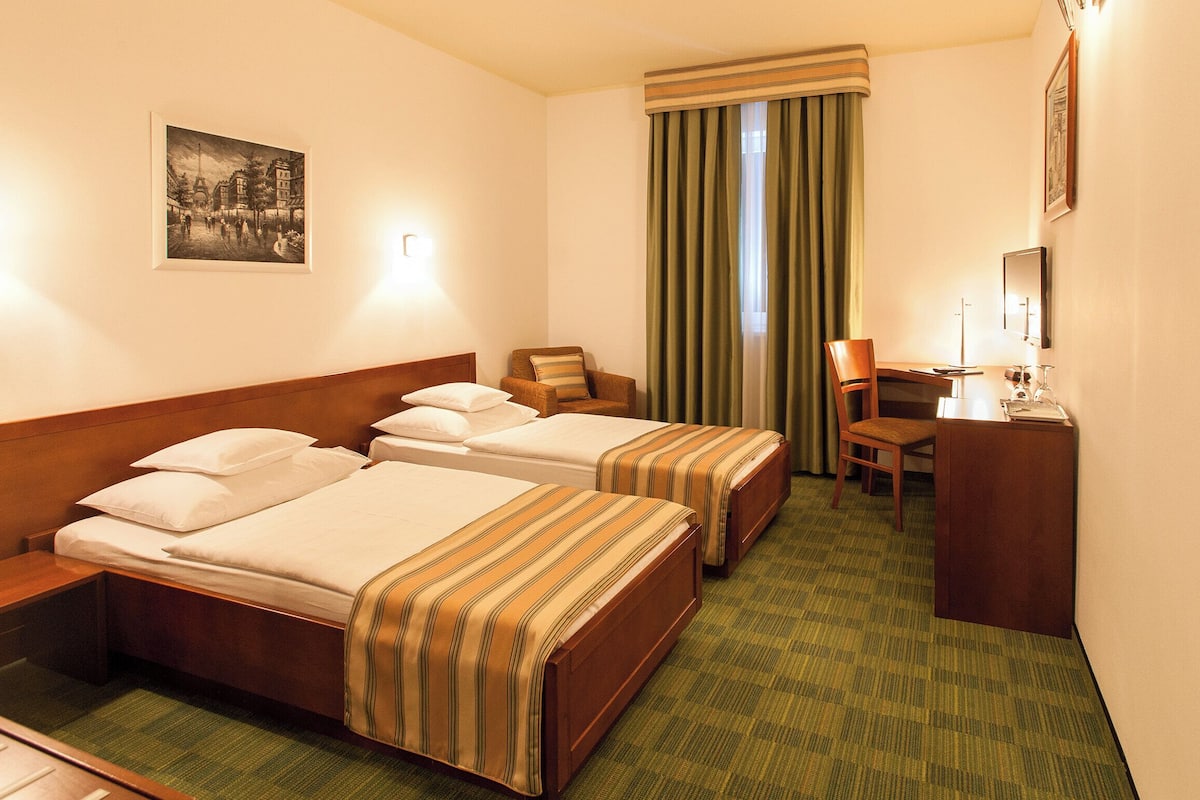 A hotel room with two beds, a desk, a chair, a mirror, and a picture on the wall.