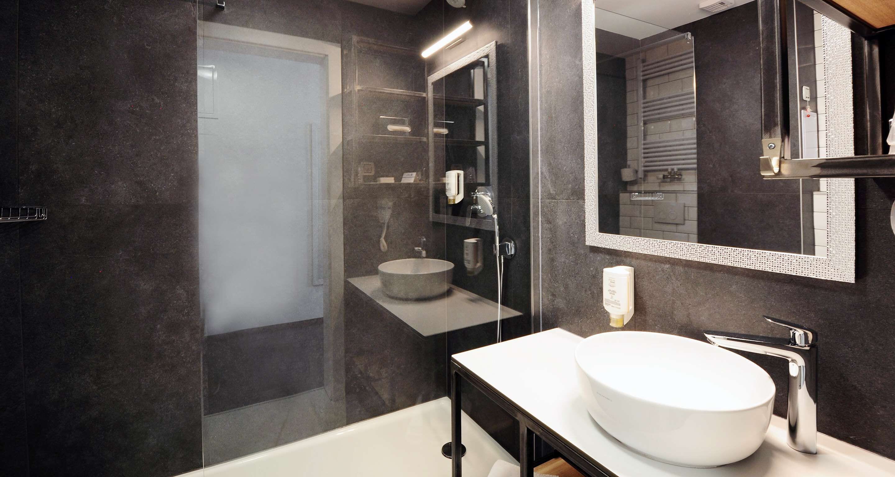Un baño moderno con ducha de vidrio, lavamanos redondo y espejo grande.