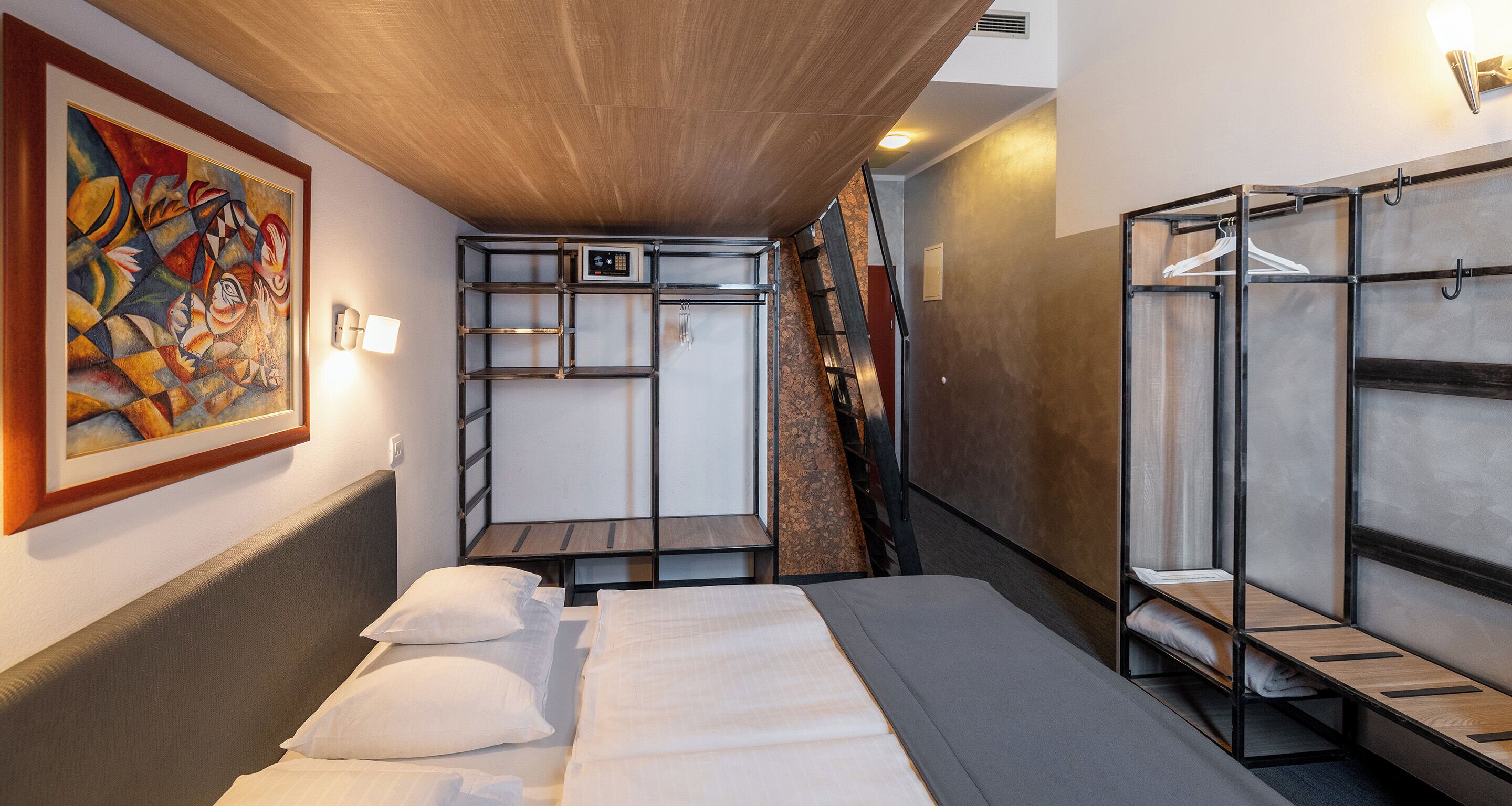 Une chambre d’hôtel compacte avec des lits superposés, un petit bureau et un tableau accroché au mur.