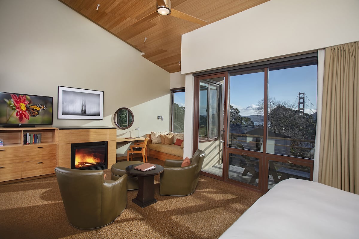 A modern hotel room with a fireplace, comfortable seating, a large window with a view of a bridge, and a flat-screen TV.