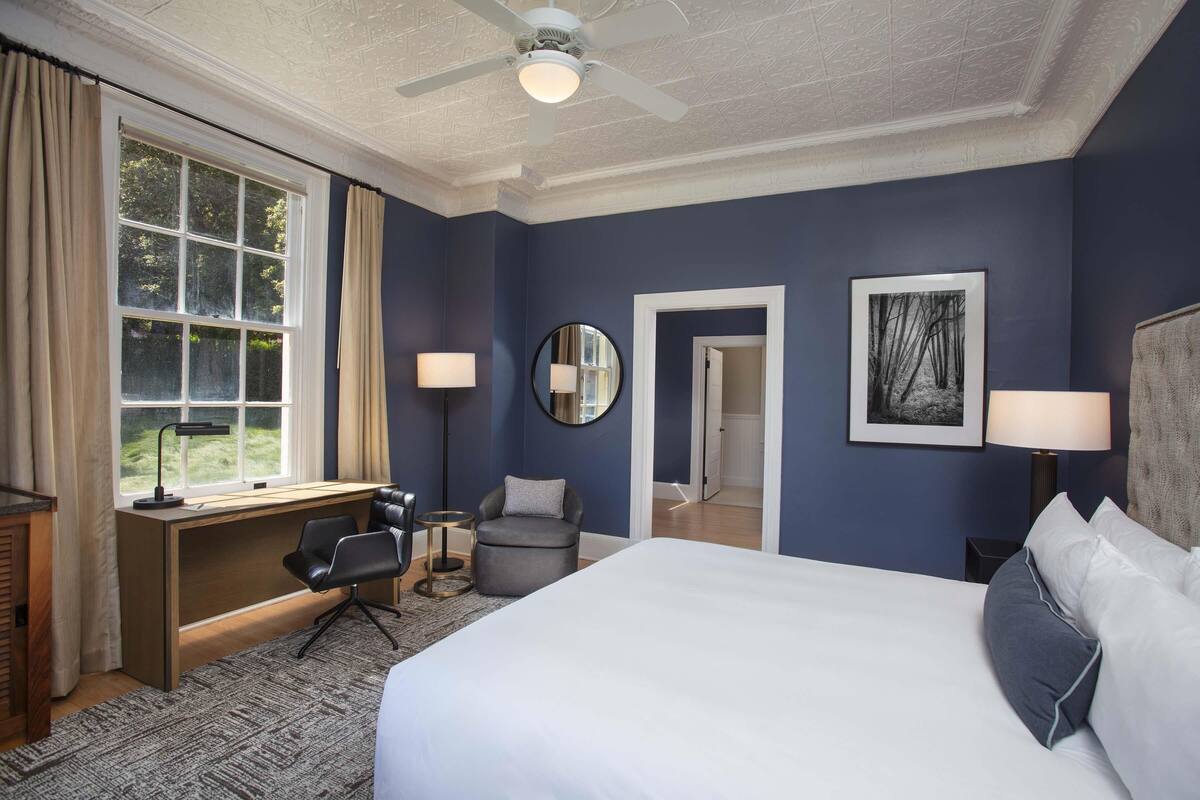 A hotel room with a bed, desk, chair, and two lamps.