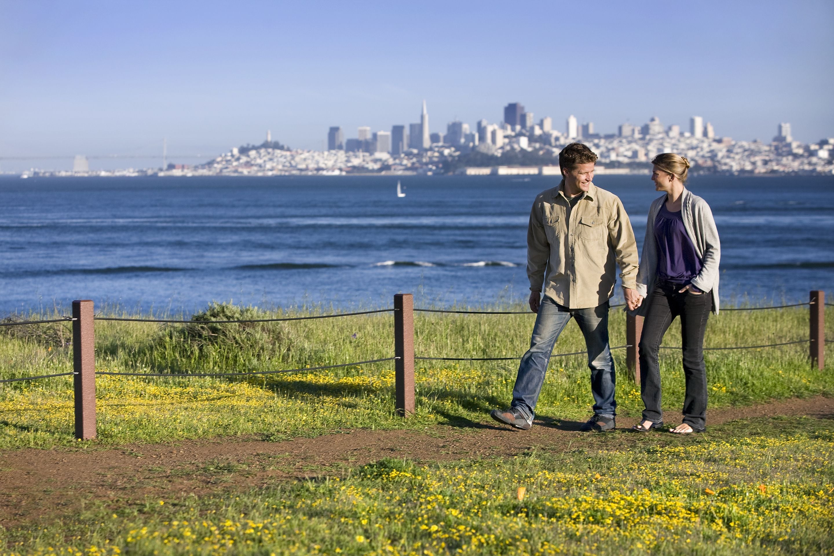A couple walking along a path with a city skyline in the background.