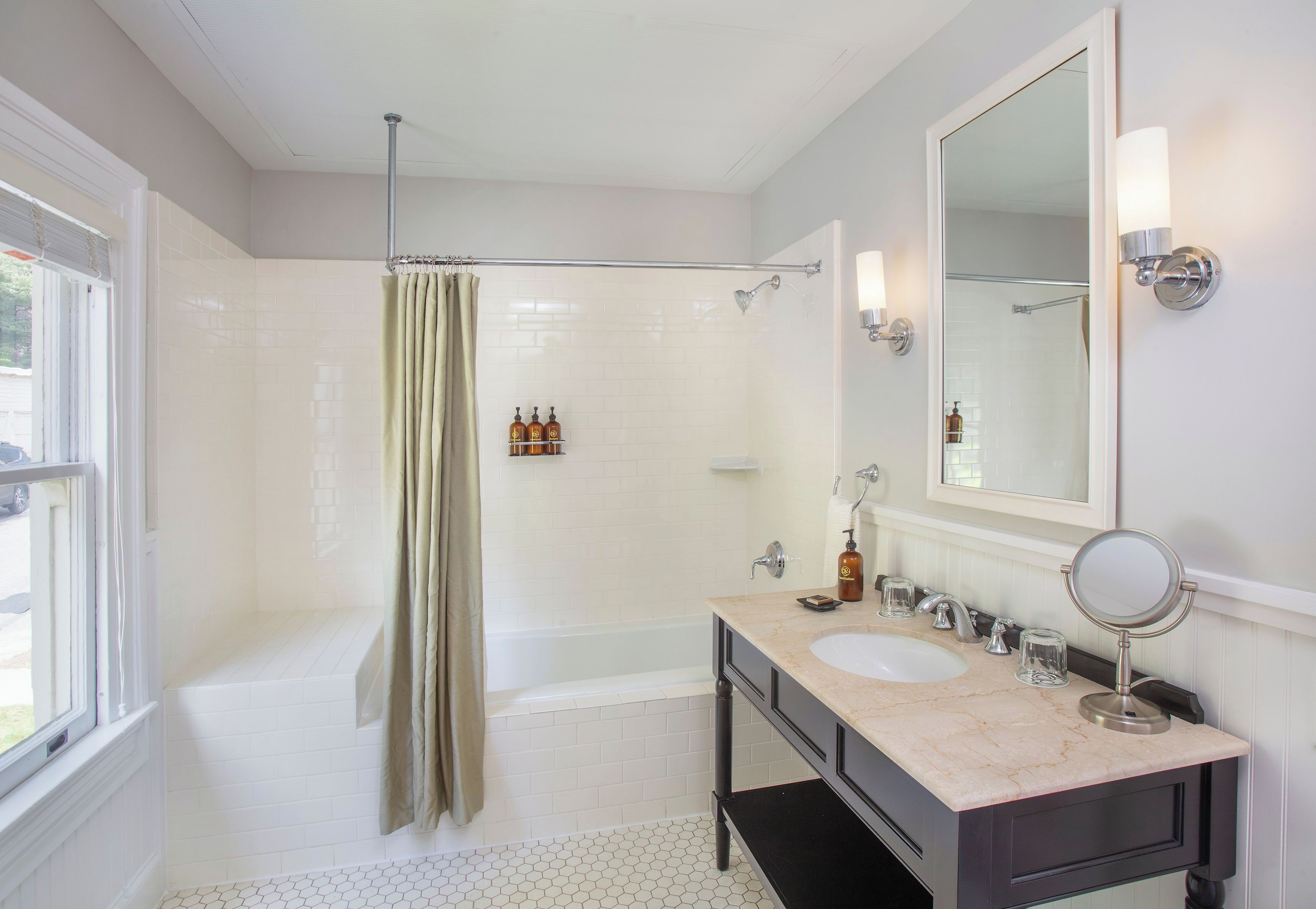 A bathroom with a bathtub, a shower, a vanity with a mirror, and a window.