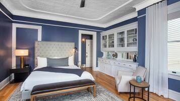 A bedroom with a large bed, a bedside table with a lamp, a small round table with a vase, and a cabinet with glass doors.