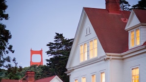 Une grande maison blanche à deux étages, avec un toit rouge, de nombreuses fenêtres et une pelouse bien entretenue.