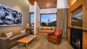 A modern living room with a sofa, armchair, and coffee table. There is a fireplace and a large window with a view of a bridge.