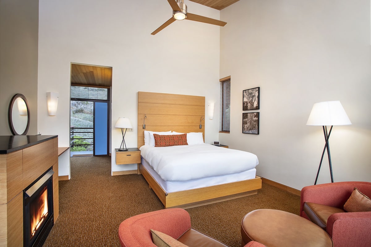 A hotel room with a bed, a ceiling fan, a fireplace, and a view of the outdoors.