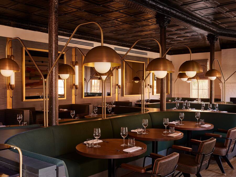 Un restaurante con mesas redondas, asientos tipo banqueta verdes e iluminación colgante de latón.