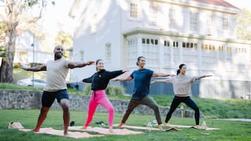 Quatro pessoas praticando yoga em tapetes, numa área gramada com um edifício ao fundo.