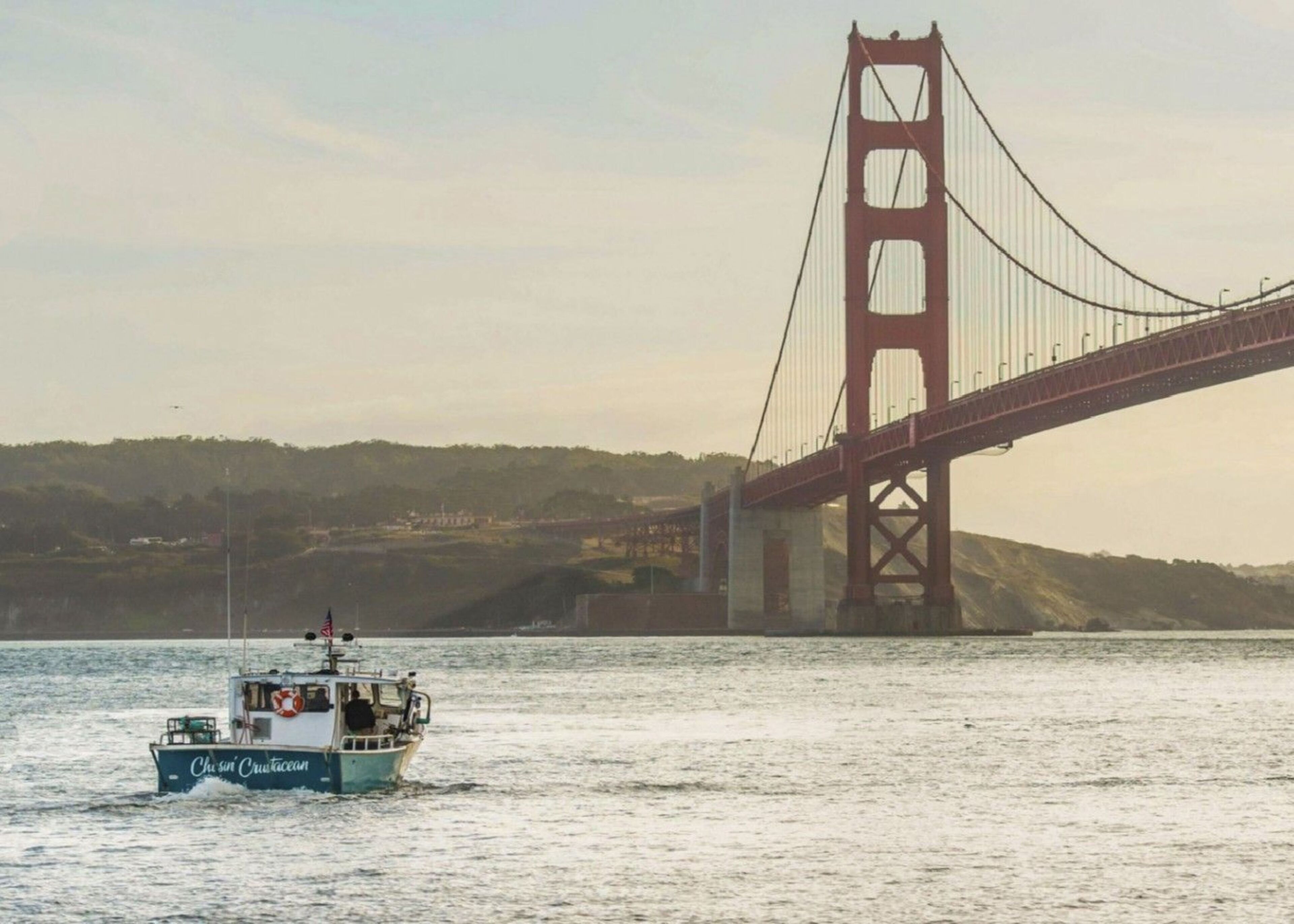 A boat named 'Chesapeake' on a body of water with a large red bridge in the background.