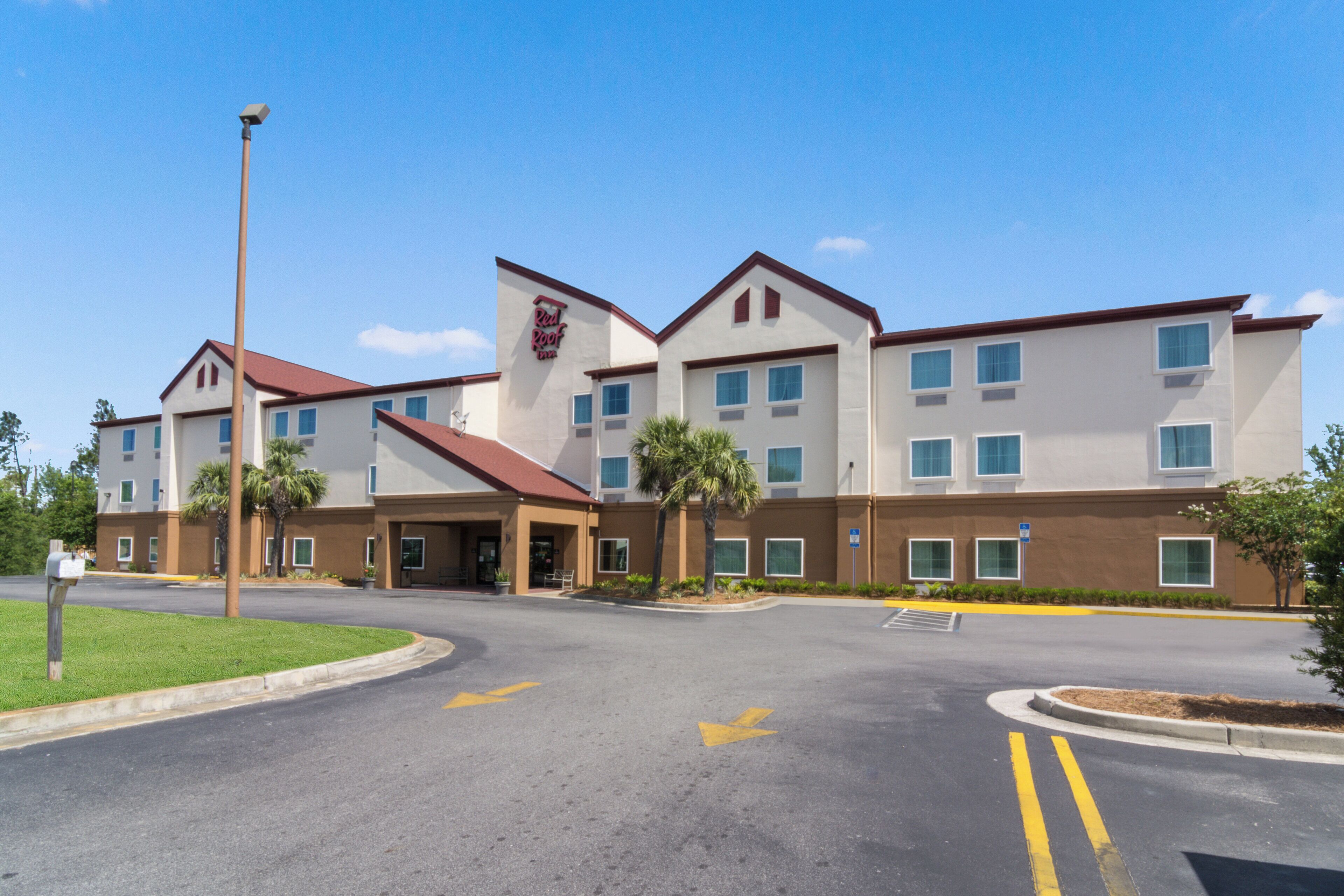 A multi-story hotel with a red roof, a prominent Red Roof Inn sign, and a parking lot with directional arrows.