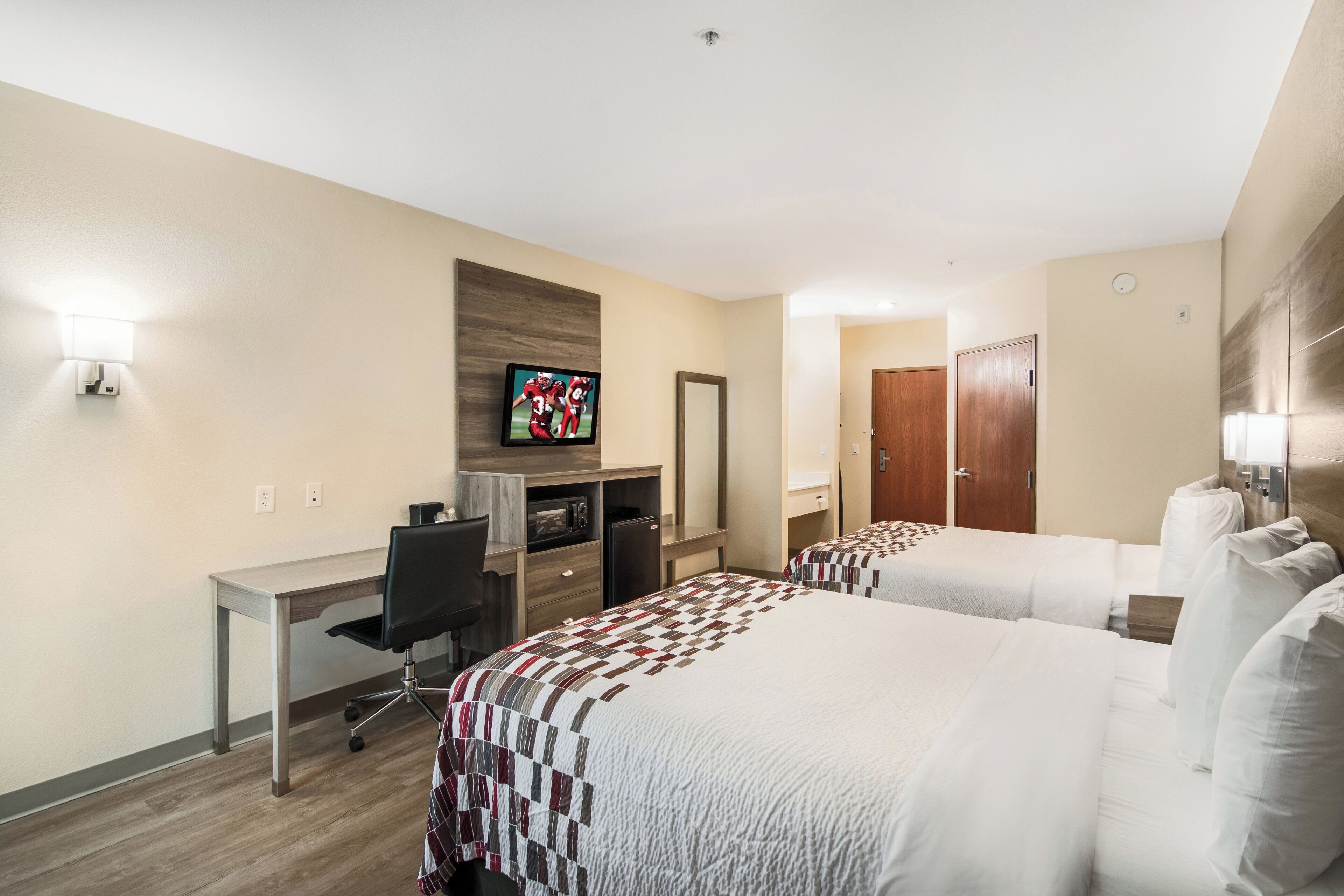 A hotel room with two beds, a desk with a chair, a television, and a microwave.