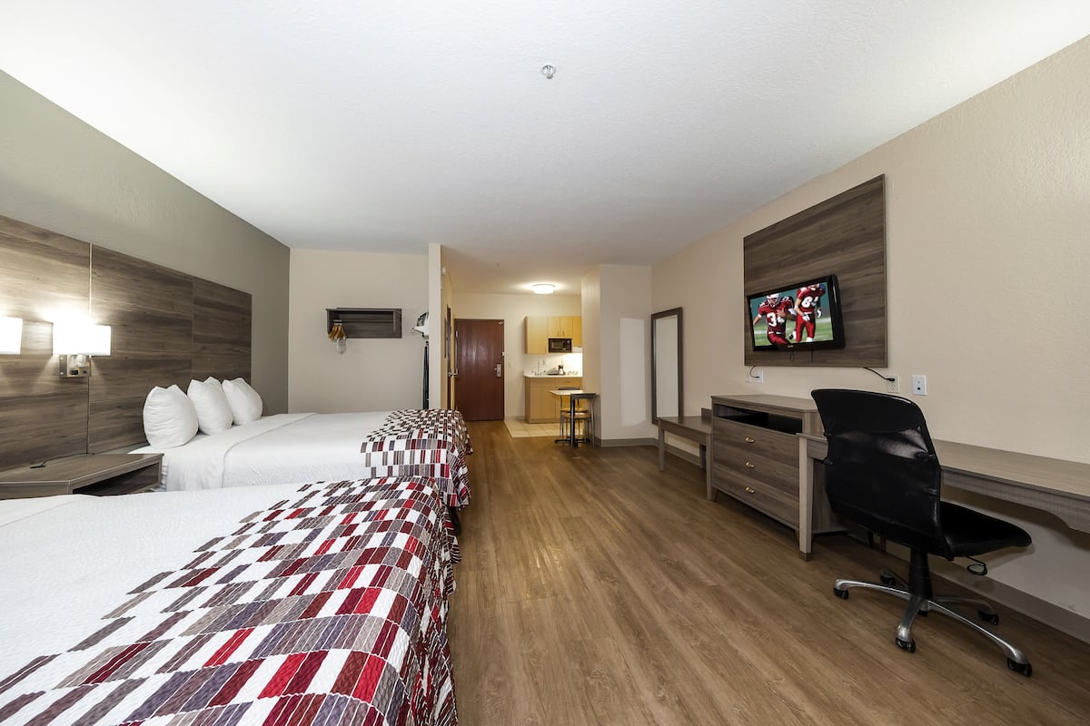 A hotel room with two beds, a desk, a chair, a TV, and a kitchenette.