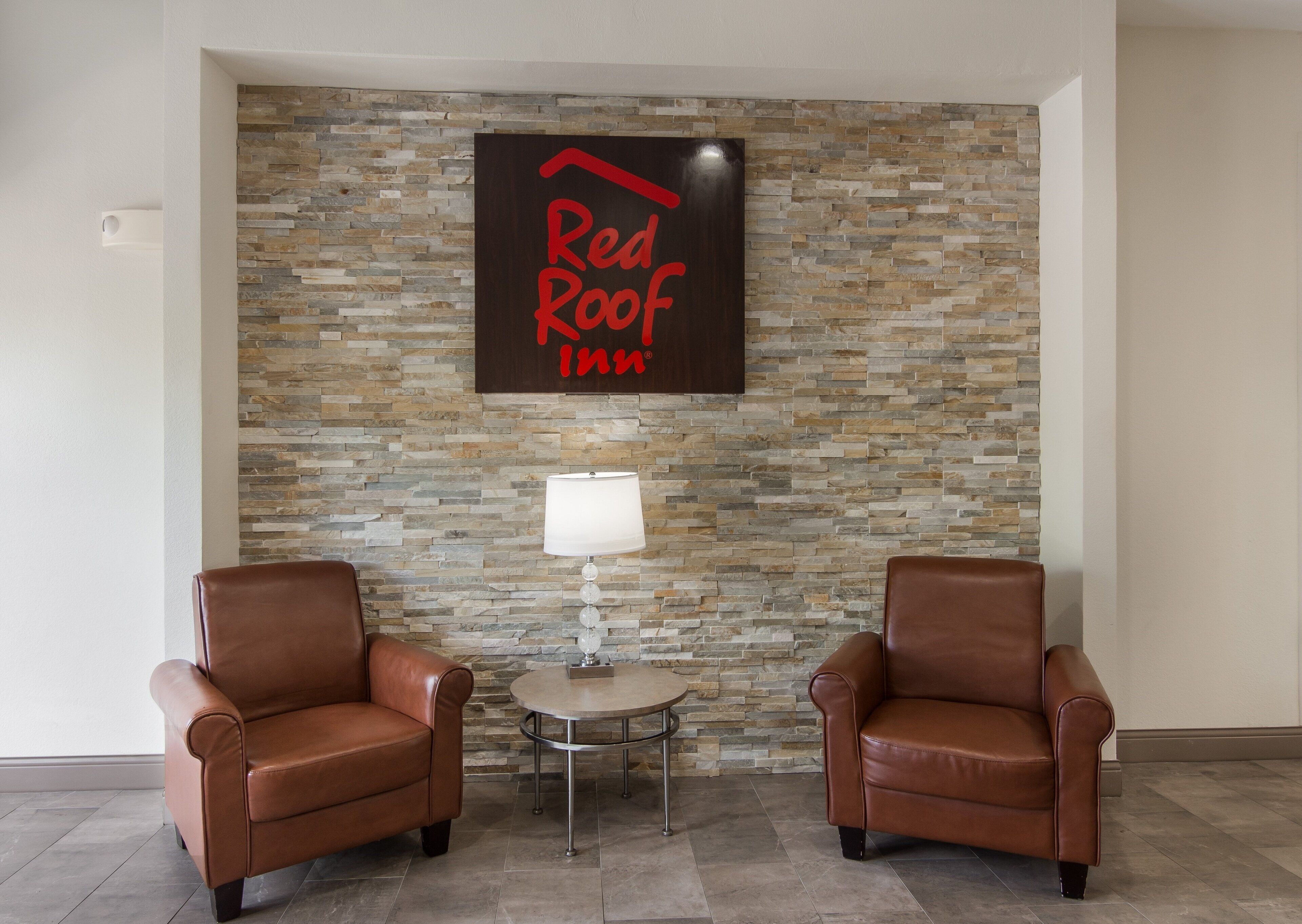 Une enseigne « Red Roof Inn » sur un mur de pierre, deux fauteuils en cuir et une petite table avec une lampe.