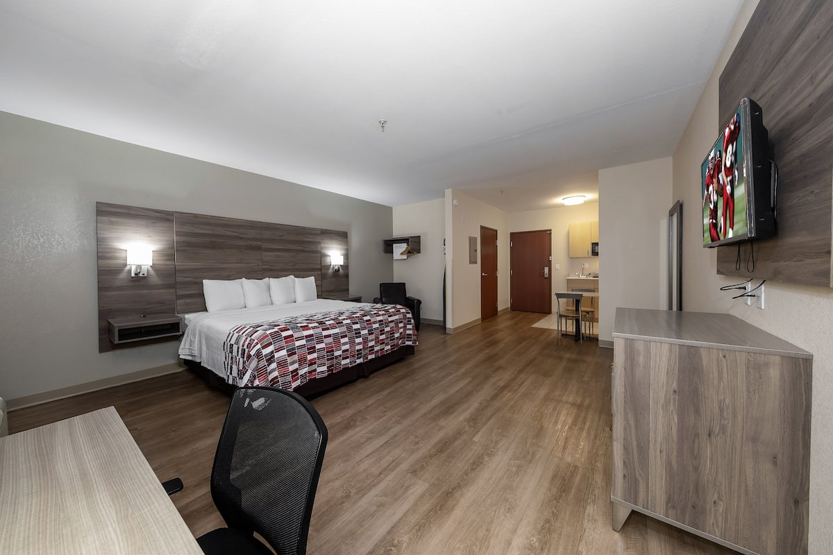 Una habitación de hotel moderna con suelo de madera, una cama con manta estampada, un escritorio con silla y un televisor montado en la pared.