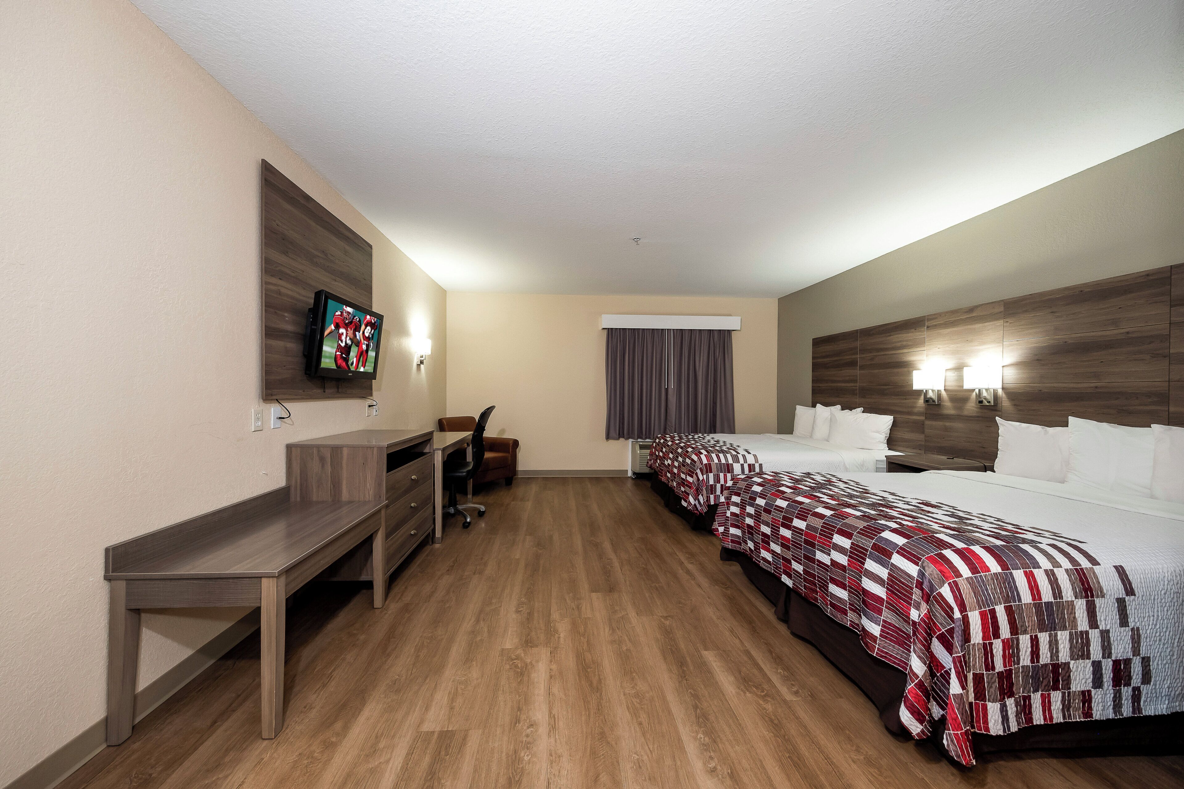 Habitación de hotel con escritorio, dos camas, televisor y ventana con cortinas.
