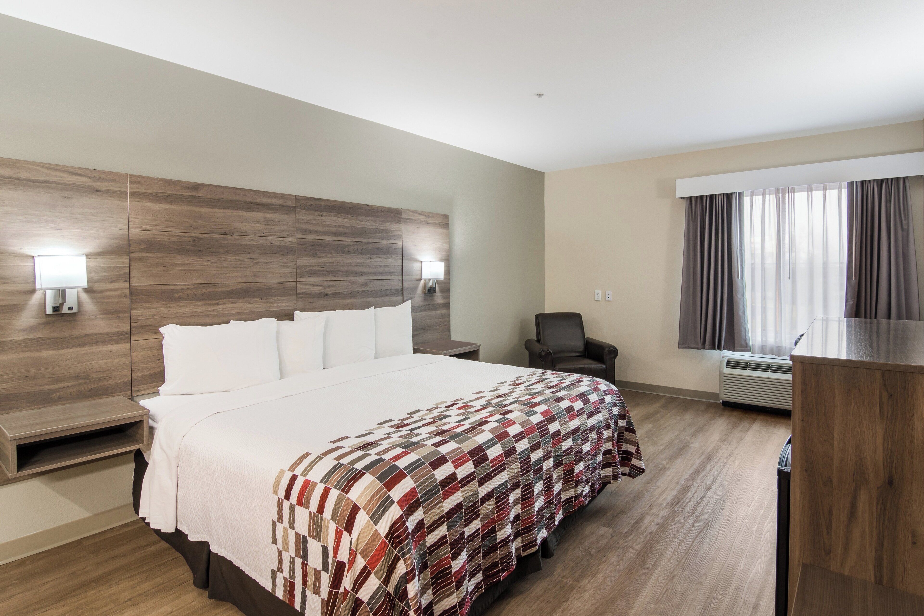 Habitación de hotel con una cama grande, un escritorio, una silla, una ventana con cortinas y un equipo de aire acondicionado.