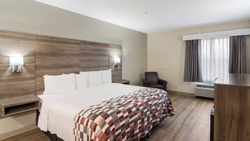 Habitación de hotel con una cama grande, un escritorio, una silla, una ventana con cortinas y un equipo de aire acondicionado.