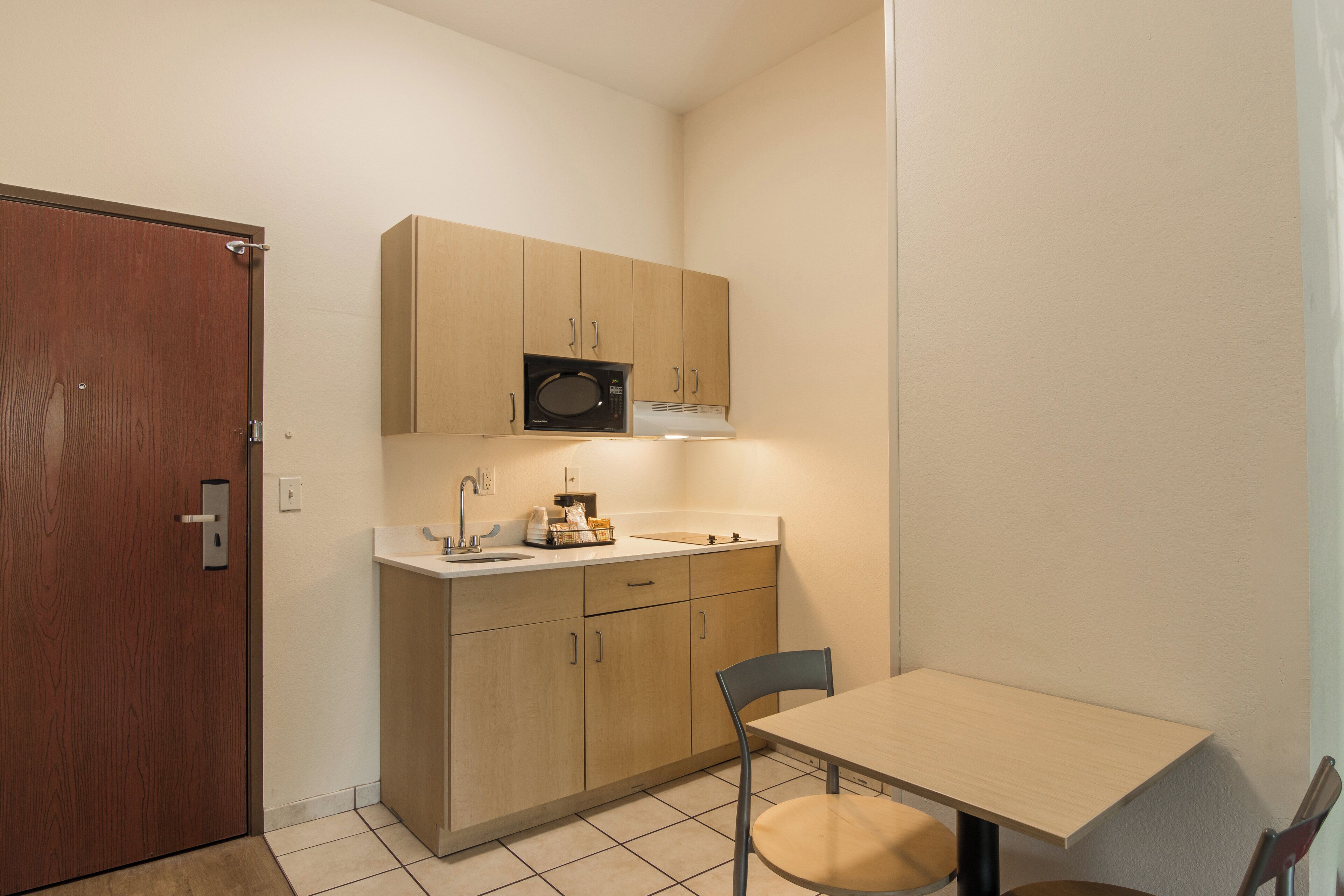 Una cocina compacta con armarios de madera, un microondas, un lavabo y una pequeña mesa de comedor.