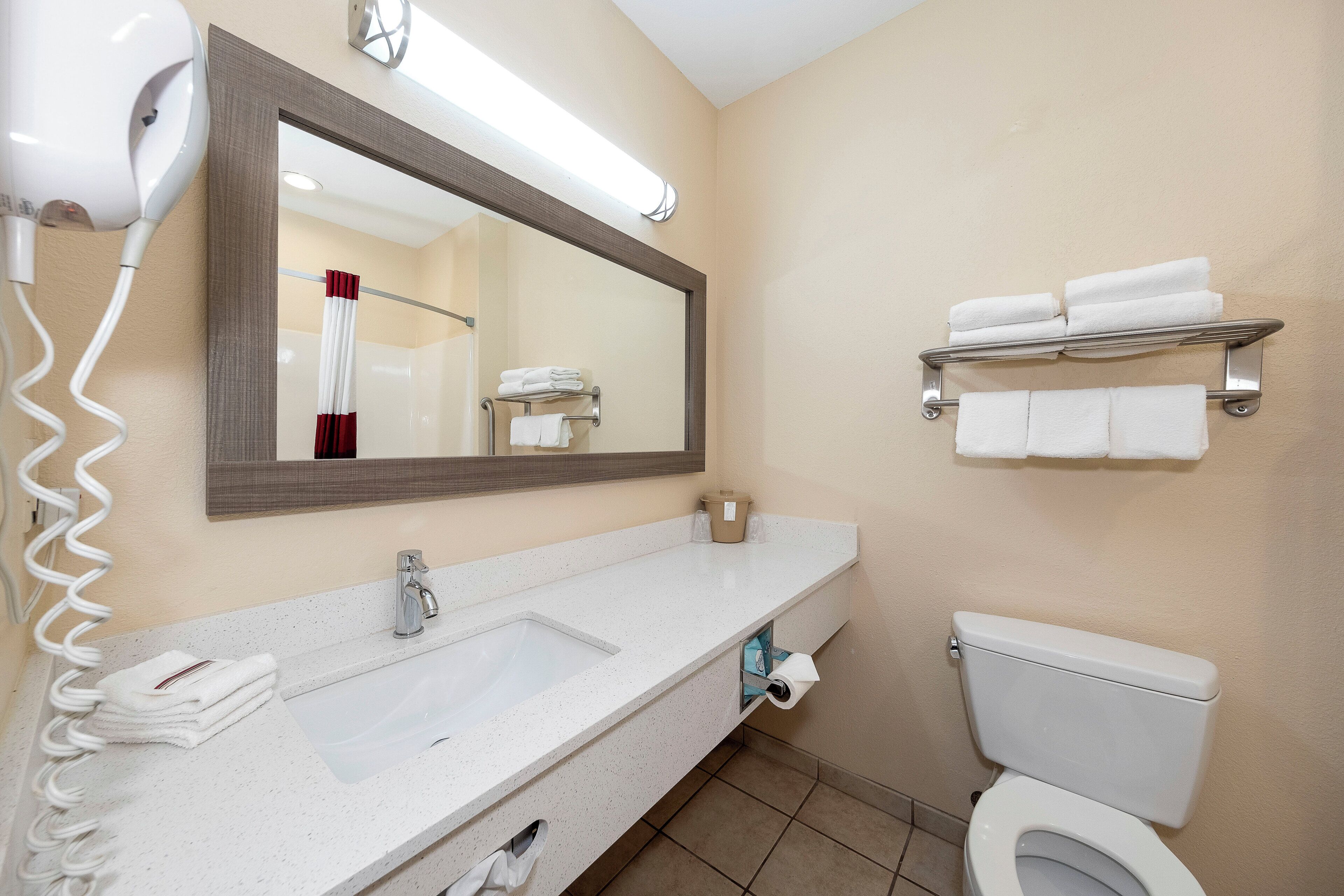Un baño con lavamanos blanco, espejo, inodoro y toallero.