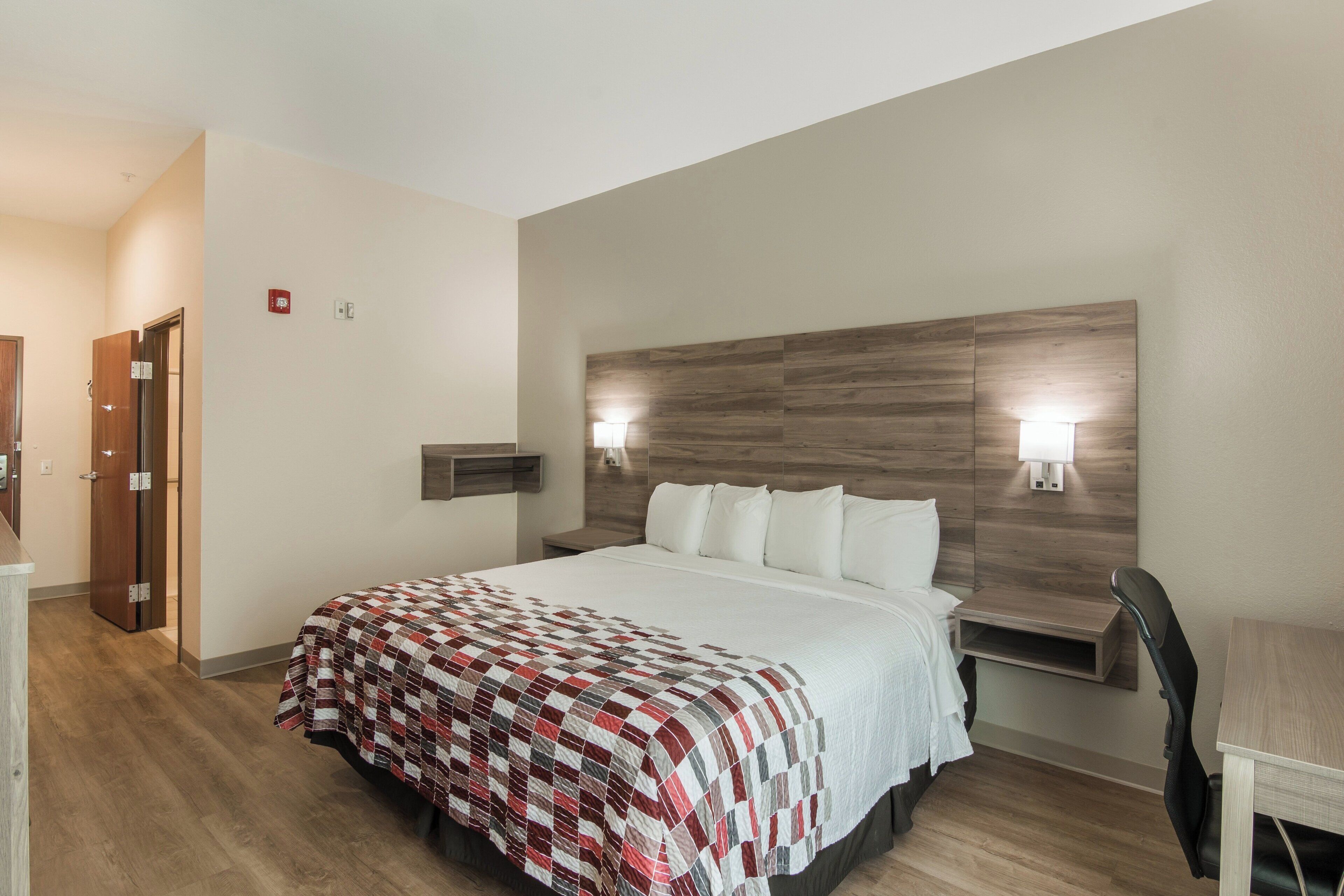 A hotel room with a large bed, a wooden headboard, two bedside lamps, a desk, and a chair.
