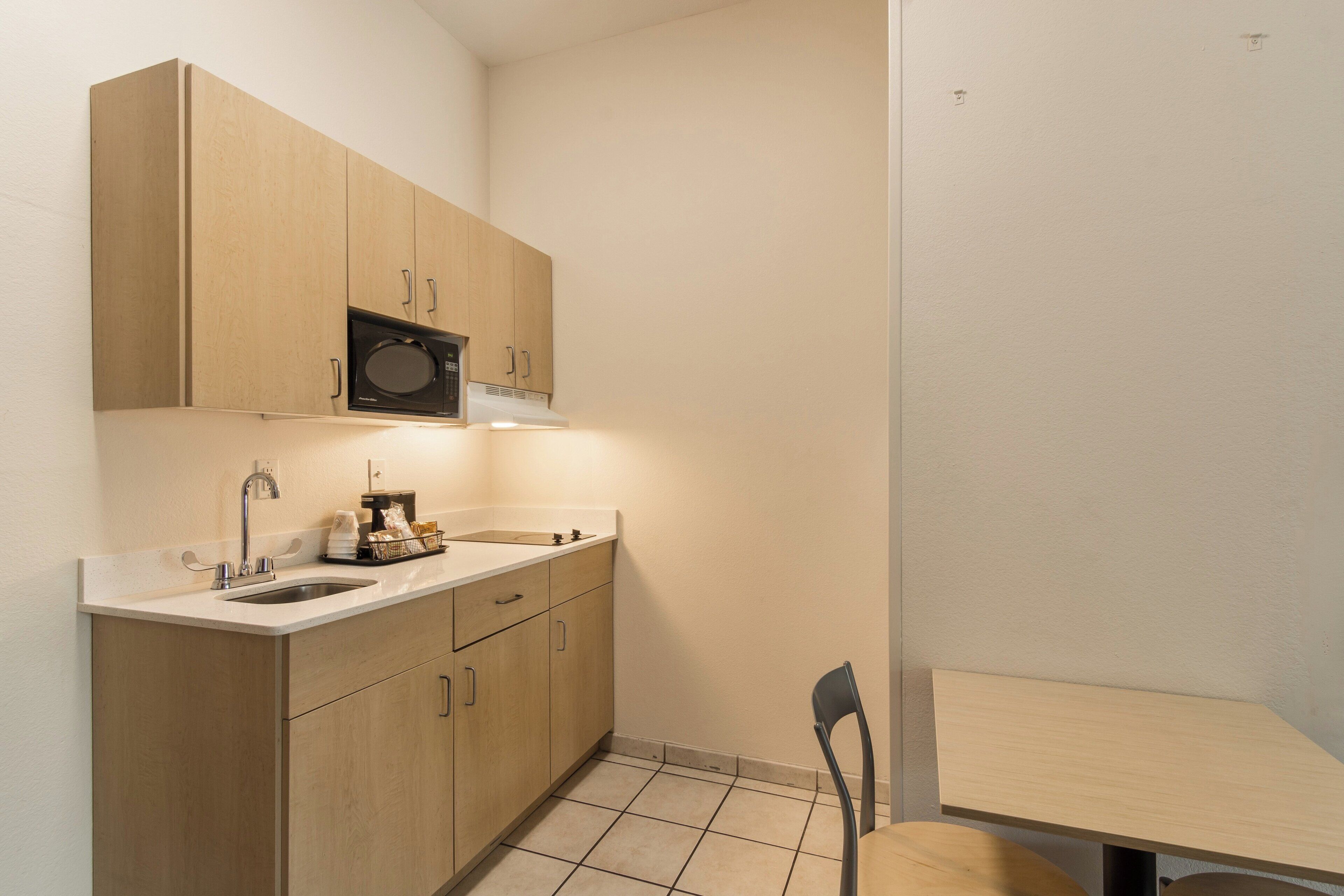 Cocina compacta con microondas, cafetera y una pequeña mesa de comedor con una silla.