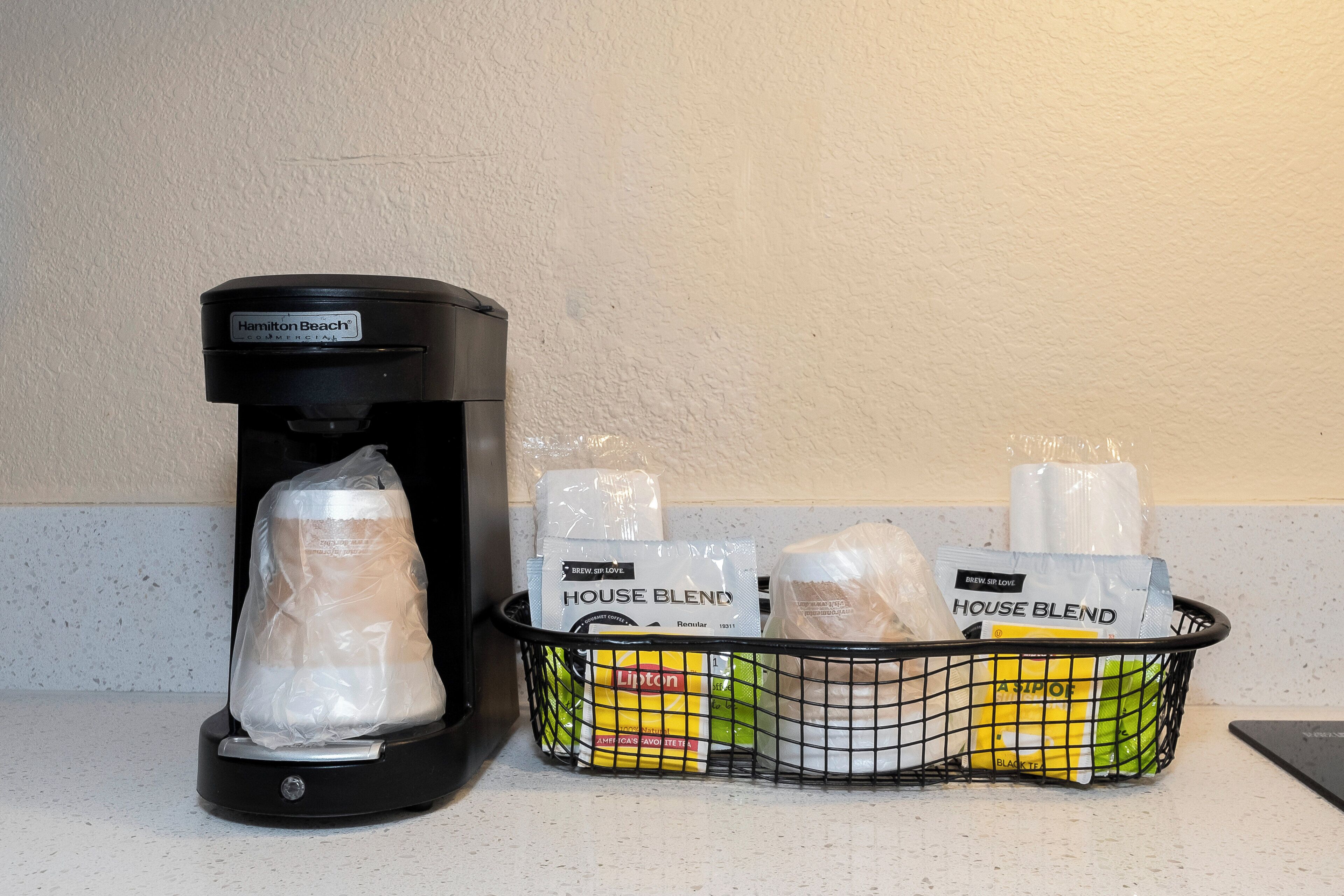 Uma cafeteira e um cesto com cápsulas de café em uma bancada.