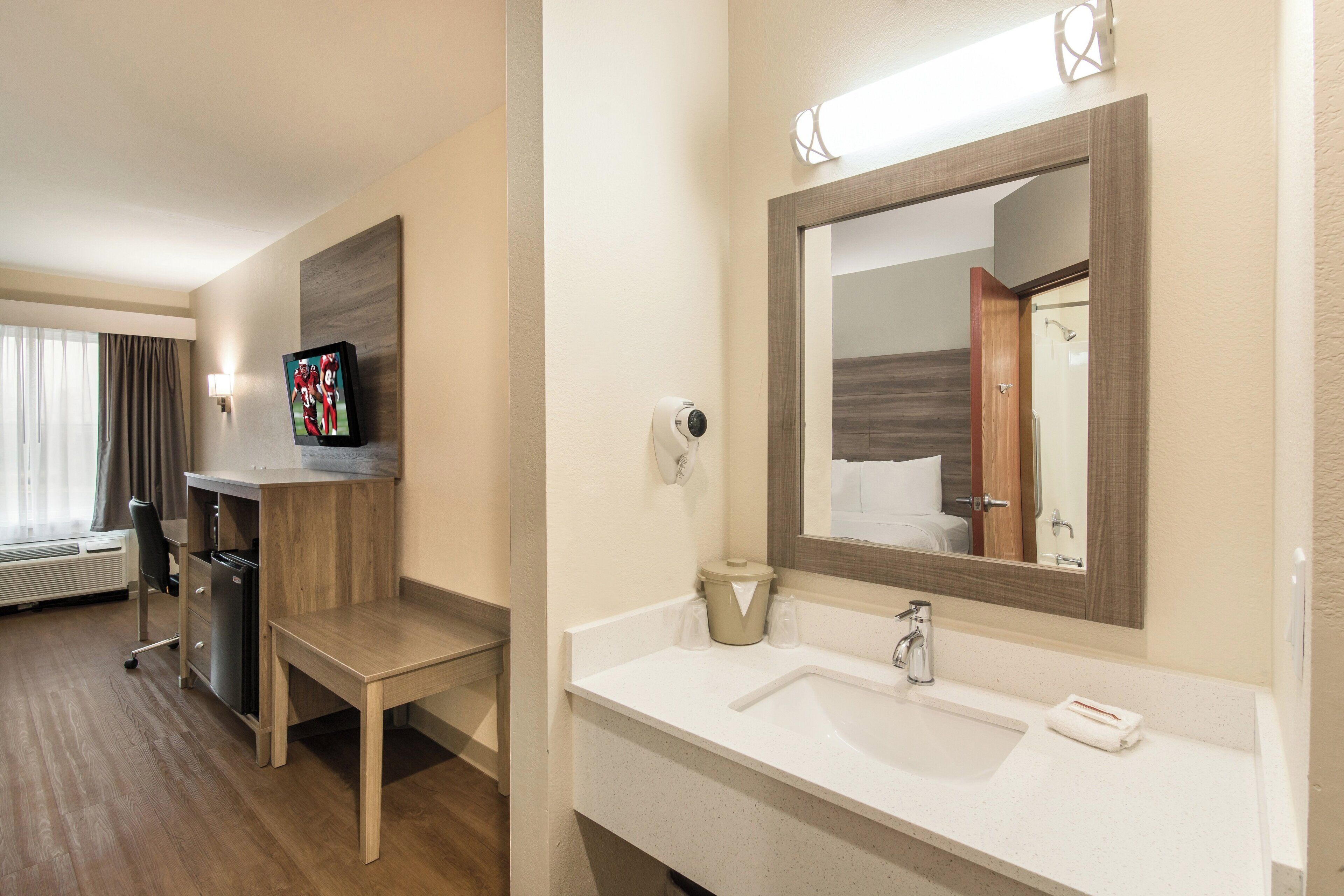 A hotel bathroom with a sink, mirror, and a television mounted on the wall.