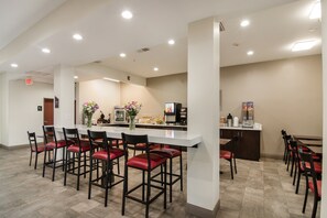 Una cocina moderna con encimera blanca, taburetes de bar tapizados en rojo, y diversos electrodomésticos y elementos decorativos.