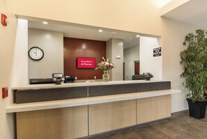 Una recepción de hotel con un reloj digital, un letrero que indica Wi-Fi gratuito y un aviso con los horarios de registro de entrada y salida.