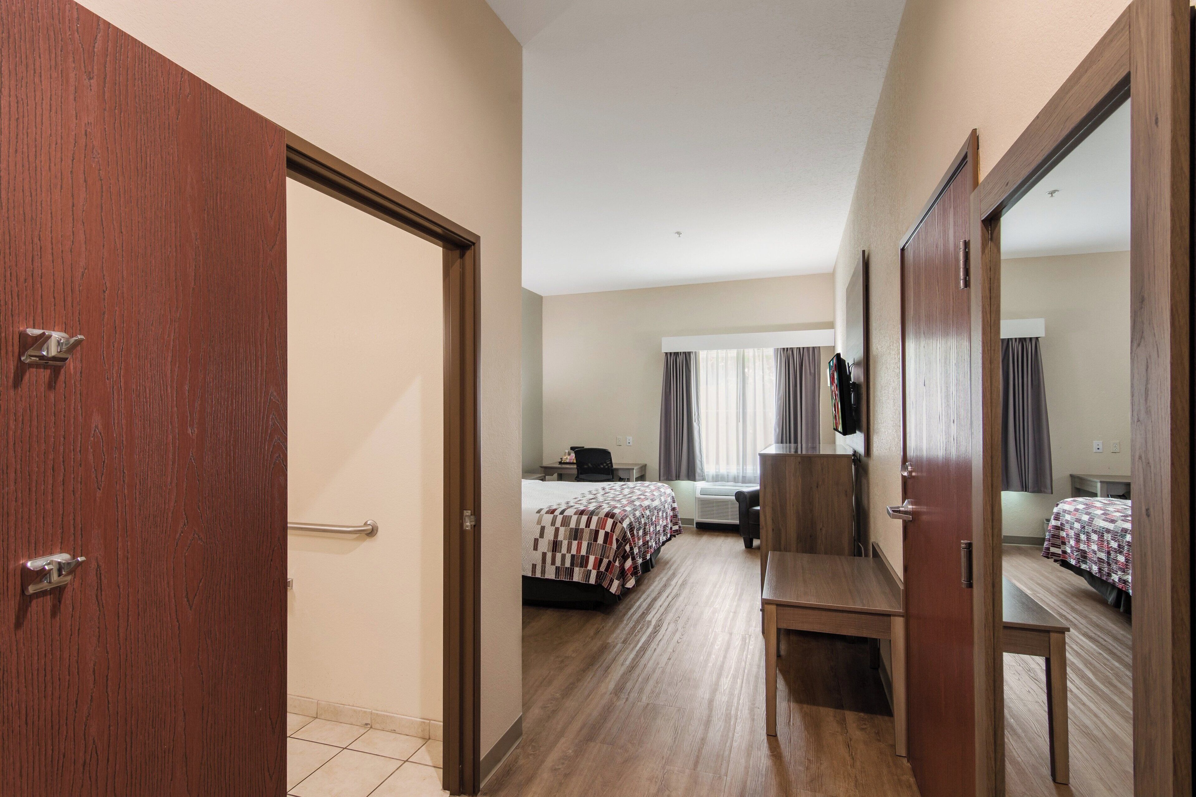 Una habitación de hotel con puerta de madera, cama con colcha estampada, escritorio con silla y un espejo grande.