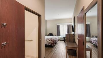 Una habitación de hotel con puerta de madera, cama con colcha estampada, escritorio con silla y un espejo grande.
