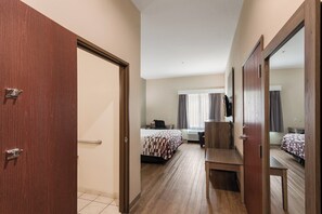 A hotel room with a wooden door, a bed with a patterned bedspread, a desk with a chair, and a large mirror. - Red Roof Inn Panama City (Panama City)