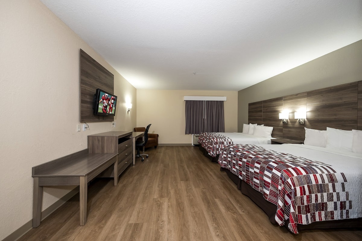 Habitación de hotel con escritorio, dos camas, televisión y ventana con cortinas.