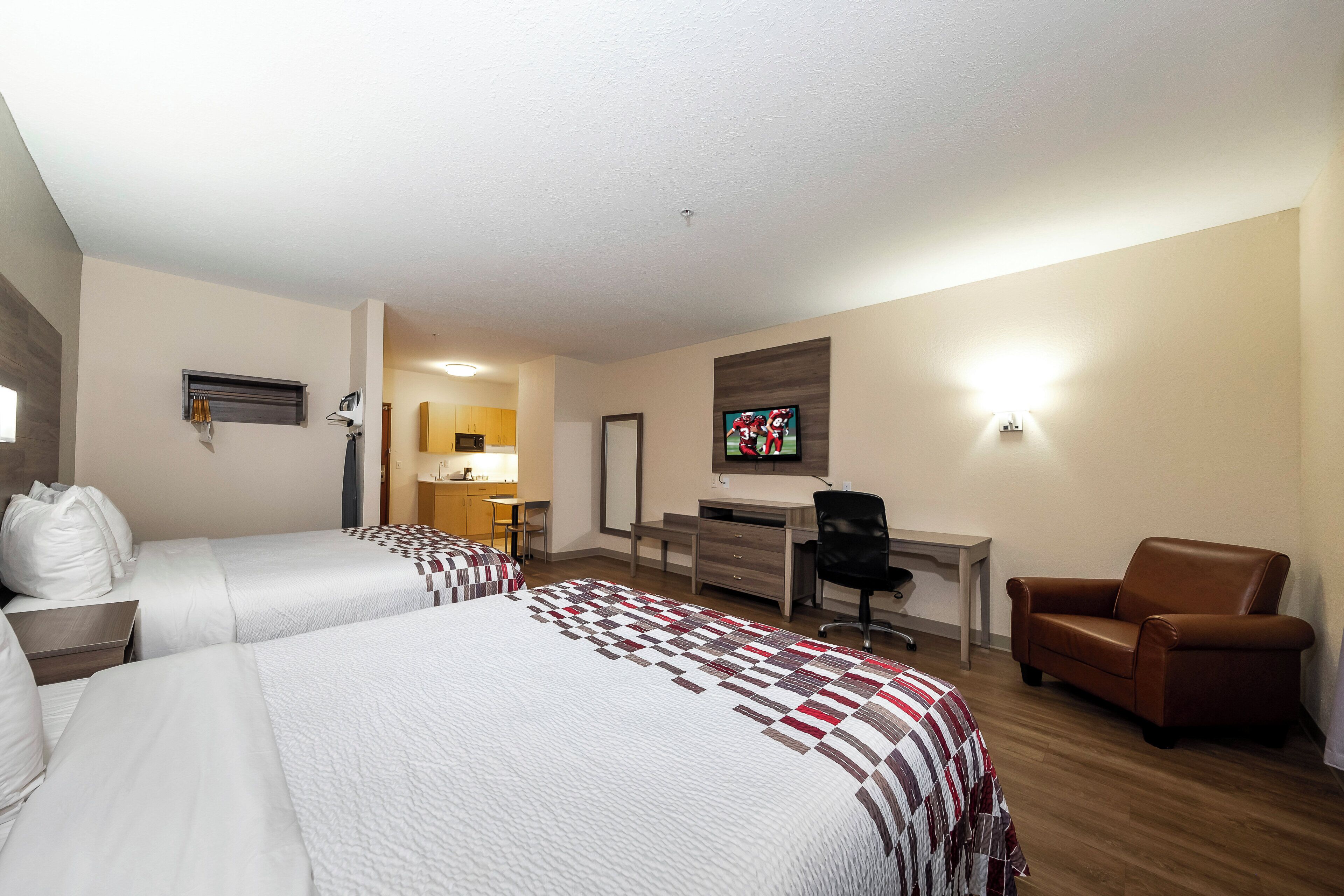 A hotel room with two beds, a desk, a chair, and a television.