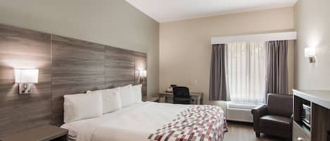 A hotel room with a large bed, a desk, a chair, and a TV.