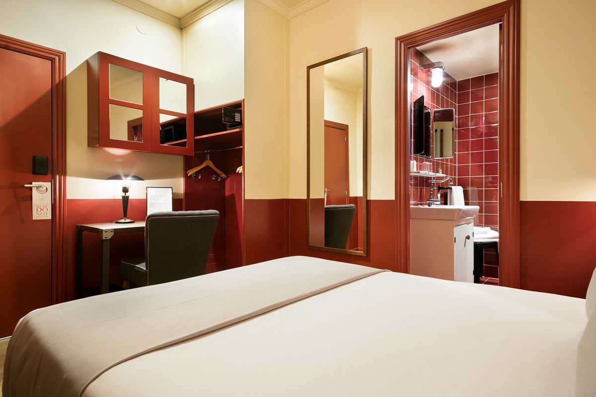 Ein Hotelzimmer mit Bett, Schreibtisch, Stuhl, Kleiderschrank und einem Badezimmer mit Spiegel und Waschbecken.