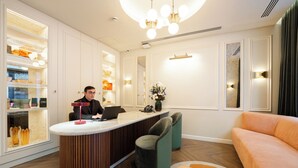 Ein Empfangsbereich mit Theke, sitzender Rezeptionistin, einer Couch und einer Blumenvase.
