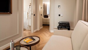 Ein Hotelzimmer mit einer Couch, einem kleinen runden Tisch mit einem Buch, einem Koffer und einem Bademantel, der im Türrahmen hängt.