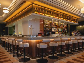 Een bar met een lange toonbank, verschillende krukken en een ruime selectie flessen en glazen.