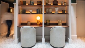 Ein Zimmer mit integriertem Schreibtisch und Regalelement, ausgestattet mit Büchern, Dekoration und einer Lampe.