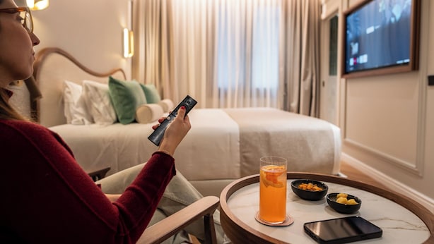 A hotel room with a bed, a TV, a glass of orange juice, and a tray with bowls of snacks. - Hotel Condal (Barcelona)