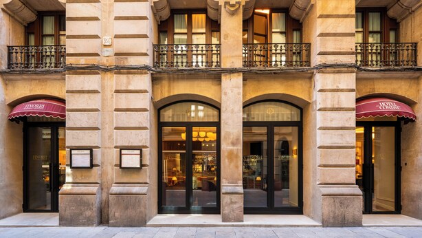 Eine Hotelscheune mit großen Bogenfenstern, einem Balkon mit schmiedeeisernen Geländern und einem roten Markisenvorbau mit dem Hotelnamen.