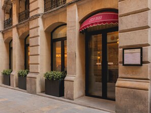 Fachada de un edificio con un restaurante llamado 'FINORRI', que presenta un toldo rojo, ventanas grandes y un menú enmarcado en la pared.