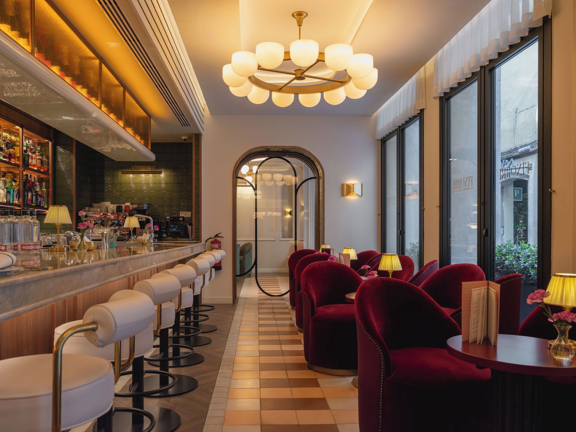 Eine Bar mit einer langen Theke, mehreren Barhocker und einem Kronleuchter.
