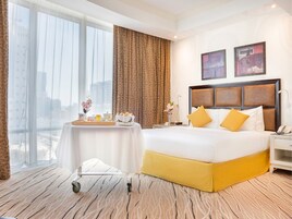 A hotel room with a large bed, a bedside table, a chair, a desk, and a view of the city.